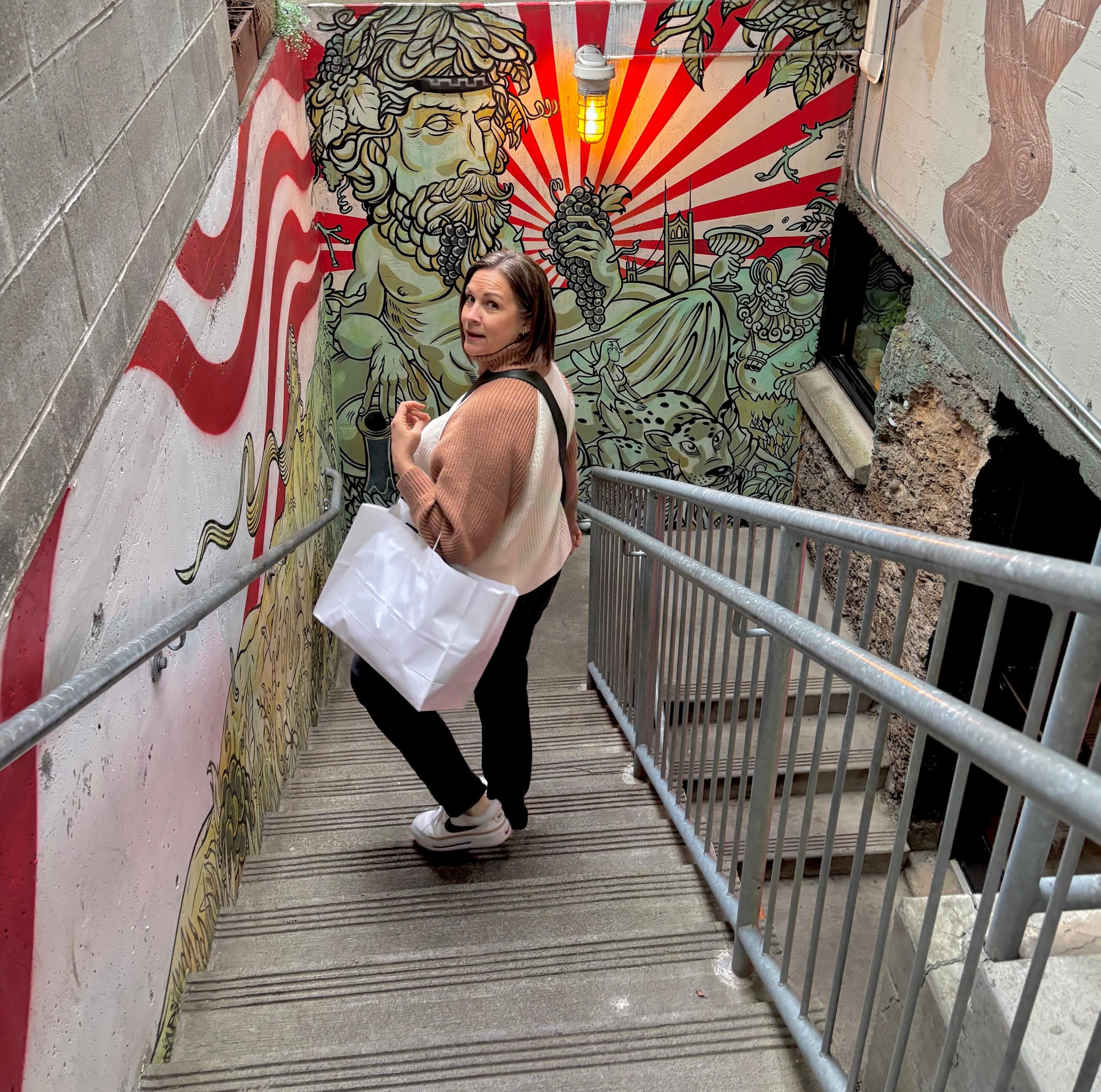 Jen standing on a stairway beside a colorful mural and building.